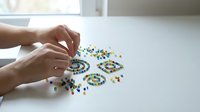 Hands arranging colorful beads in circular patterns on white surface, craft and jewelry making activity for design and creative projects.