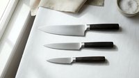 Professional kitchen knife set with three sharp blades and dark wooden handles on white cutting board, culinary tools for cooking and food preparation.