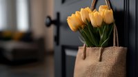 Fresh yellow tulips in rustic burlap bag hanging on black door handle, creating cozy spring home decoration atmosphere with soft natural lighting.