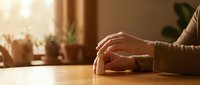 Relaxed hands resting on wooden table in warm sunlit room with plants creating peaceful morning atmosphere for meditation and mindfulness concepts.