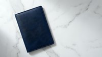 Navy blue leather notebook or journal lying closed on white marble surface for business planning and professional writing tasks.