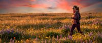 Woman jogging through wildflower meadow at sunset, wearing athletic gear, surrounded by purple and yellow blooms, golden hour landscape for fitness and wellness content.
