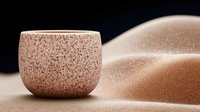 Minimalist ceramic bowl with speckled texture against smooth sandy dunes background creates zen atmosphere for wellness and spa designs.