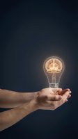 Male hand holding glowing light bulb with brain illustration inside against dark background, representing innovation, creativity, and intelligent ideas for business and technology concepts.