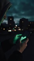 Person wearing dark hoodie holding smartphone with glowing neon heart icon against blurred nighttime cityscape with illuminated buildings and bokeh lights.