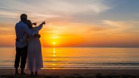 Romantic couple silhouette embracing on beach at golden sunset with ocean waves and colorful sky for wedding anniversary celebration.