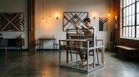 Young professional man working on laptop in modern industrial office space with exposed brick walls, geometric wall art, and warm pendant lighting.