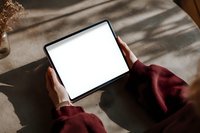Person holding digital tablet with blank white screen in burgundy sweater at wooden table with soft natural lighting.