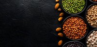 Assorted legumes, nuts and grains in black ceramic bowls on dark stone background. Healthy protein sources and vegan food ingredients for cooking.