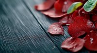Red rose petals scattered on dark wooden surface with water drops and green leaves create romantic mood, soft focus with copy space for Valentine designs.
