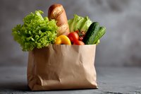 Fresh groceries in paper bag with bread, lettuce, tomatoes, cucumber and orange against gray background, ideal for healthy eating and food delivery concepts.