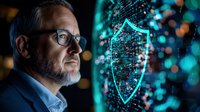Mature businessman with glasses looking at glowing cybersecurity shield hologram visualization against dark background with digital network connections.