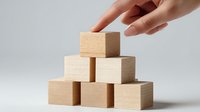 Female hand stacking wooden blocks in pyramid formation on white background, symbolizing business growth, construction, and strategic planning.