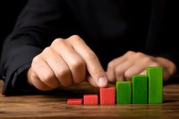 Business person arranging wooden blocks in ascending order showing growth trend on wooden desk, red to green progression demonstrates positive performance.