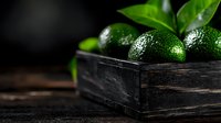 Fresh green limes with water drops in rustic dark wooden box against black background, dramatic lighting with green leaves, food photography.