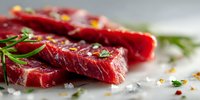 Fresh raw beef steaks seasoned with herbs, salt, and spices on gray surface, ready for cooking.