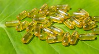 Golden vitamin E oil capsules scattered on fresh green leaf surface for natural health and wellness supplement concepts.