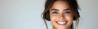 Young woman with radiant smile wearing wireless headphones against light background, casual style with natural makeup and updo hairstyle for music and lifestyle content.