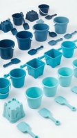 Collection of blue plastic beach toys and sand buckets arranged on white background, including pails, shovels, and castle molds for summer play.