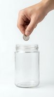 Male hand dropping coin into empty glass jar against white background, representing savings, investment, and financial planning.