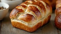 Freshly baked golden challah bread with shiny crust and soft texture on wooden surface, traditional Jewish braided loaf for Sabbath meals.