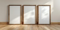 Three empty wooden picture frames with white mats leaning against wall on hardwood floor, casting soft shadows in minimalist interior setting.