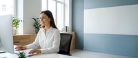 Professional Asian businesswoman working on laptop in modern office environment with natural lighting and plants for corporate presentations.