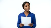 Young African American woman in professional blue shirt holding blank white document or clipboard against white background, suitable for corporate, business, and recruitment marketing materials.
