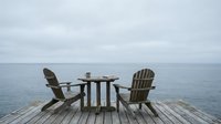 Two wooden lounge chairs on a weathered dock facing calm ocean waters, ideal for relaxation, travel, and lifestyle concepts.