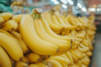 Fresh ripe yellow bananas arranged in rows at grocery store produce section, selective focus on foreground bunch with blurred background.