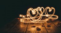 Light painting heart shapes created with sparklers on wooden surface in dark romantic setting for Valentine's Day celebrations and love concepts.