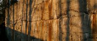 Aged stone wall with rust streaks and warm golden light casting dramatic shadows, showcasing natural texture and weathered surface detail.