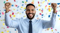 Young African American businessman celebrating success with raised arms against colorful confetti background, expressing joy and achievement in professional setting.