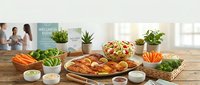 Healthy meal preparation spread with fresh vegetables, herbs, and cooked dishes on wooden table in bright kitchen setting for nutritious cooking concepts.