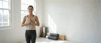 Woman in her 30s with medium skin tone practicing yoga in a bright, minimalist studio space with exercise equipment nearby.