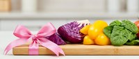 Fresh vegetables with pink gift bow on wooden tray, ideal for healthy eating, nutrition, organic food marketing, recipe blogs, and culinary content creation.
