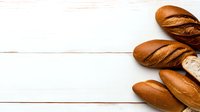Fresh crusty bread loaves arranged on white wooden background with copy space for text, food photography styling for bakery marketing.
