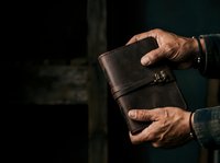 Close-up of male hands holding empty brown leather wallet against dark background, depicting financial hardship, bankruptcy, or money shortage concept.