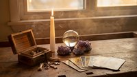 Mystical fortune telling setup with tarot cards, crystal ball, candle and wooden chest on rustic table for divination and spiritual guidance sessions.