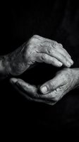 Elderly wrinkled hands cupped together in protective gesture on dark background. Black and white monochrome photography showing aging, care and human connection.