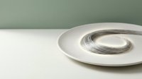 Minimalist composition featuring a white ceramic plate with a single brushstroke of black paint creating an abstract circular design, set against a neutral gray and white background for modern art and design projects.