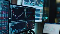 Financial trading screens showing stock market charts and graphs in dark office environment. Multiple monitors display real-time market data analysis for investment decisions.