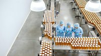 Pharmaceutical workers in protective suits monitoring automated production line with bottles in sterile manufacturing facility for quality control.