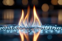 Blue gas flame burning on modern stove with bokeh lights reflection on glass surface, close up macro shot showing detailed fire pattern.