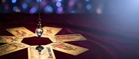Fortune telling tarot cards spread with crystal pendulum on mystical table with bokeh lights creating magical atmosphere for divination readings.