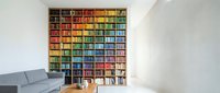 Modern home library with colorful rainbow organized bookshelf wall featuring thousands of books arranged by color spectrum in contemporary living room interior.
