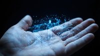 Human hands cupped together holding glowing blue digital brain with neural network connections and particles on dark background for AI technology concepts.