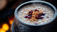 Creamy oatmeal porridge topped with cranberries and pine nuts in rustic ceramic bowl against dark background with warm glowing lights. Cozy breakfast setting.