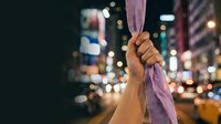 Person holding purple fabric against blurred urban nighttime cityscape with bokeh lights. Suitable for motivation, determination, resilience, and urban lifestyle concepts.