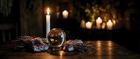 Mystical crystal ball on wooden table with amethyst geodes, dried lavender, and glowing candles in dark atmospheric setting.